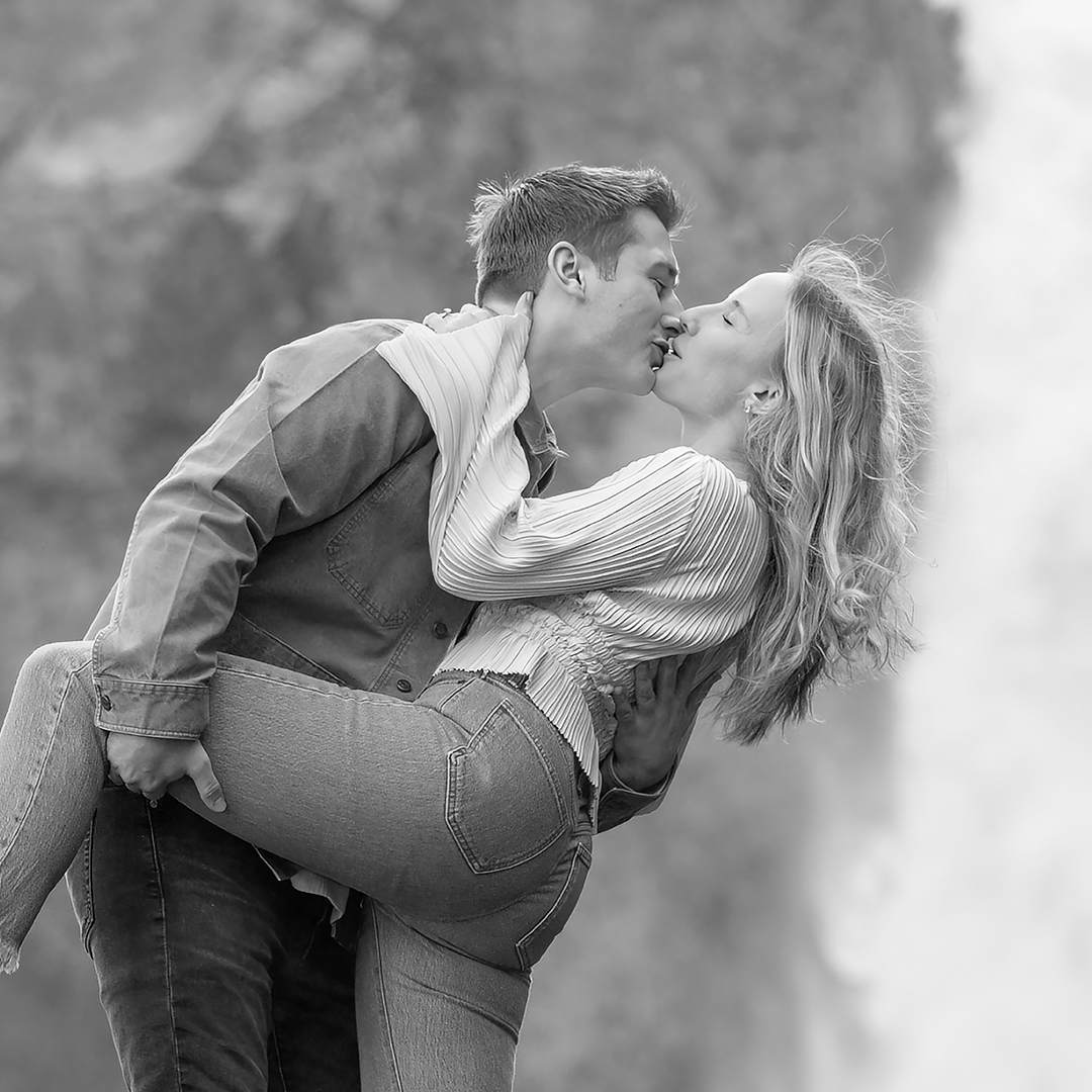 Waterfall dip. Couple is standing on a rock while the man dips the woman back and kisses her. 