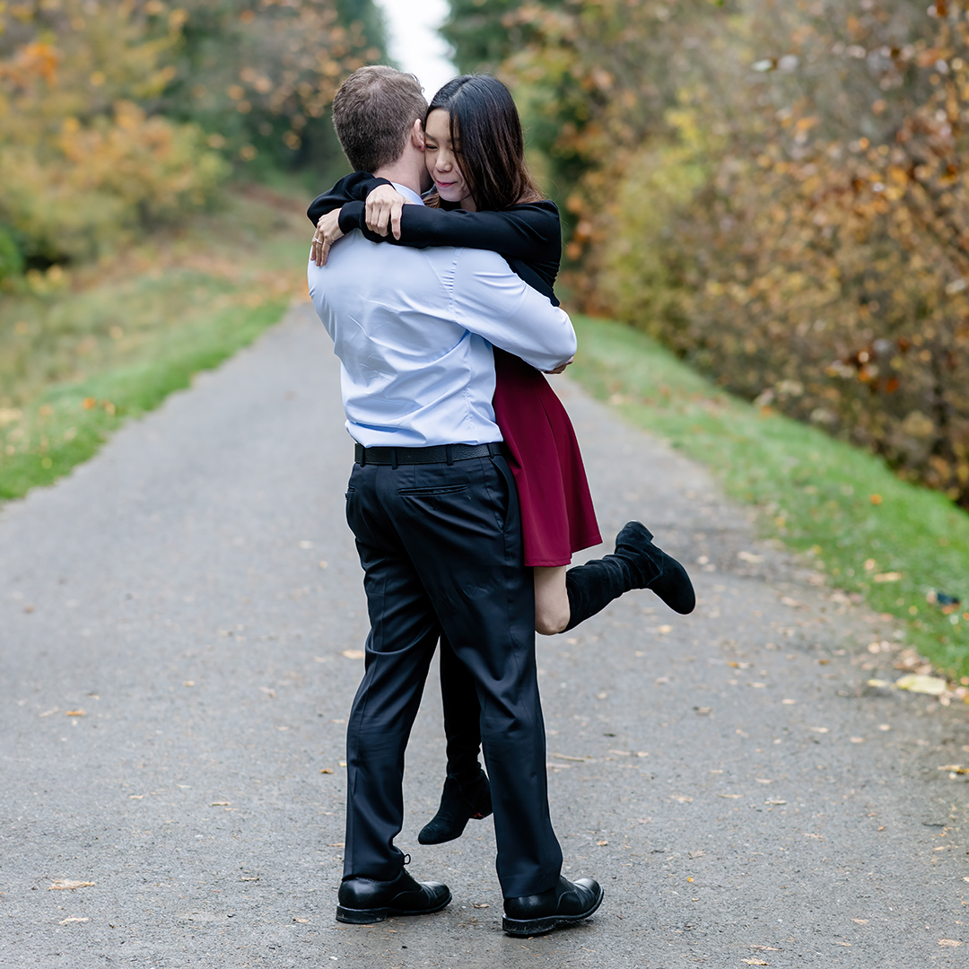 Man swings his fiancé  around while walking on a paved path. 