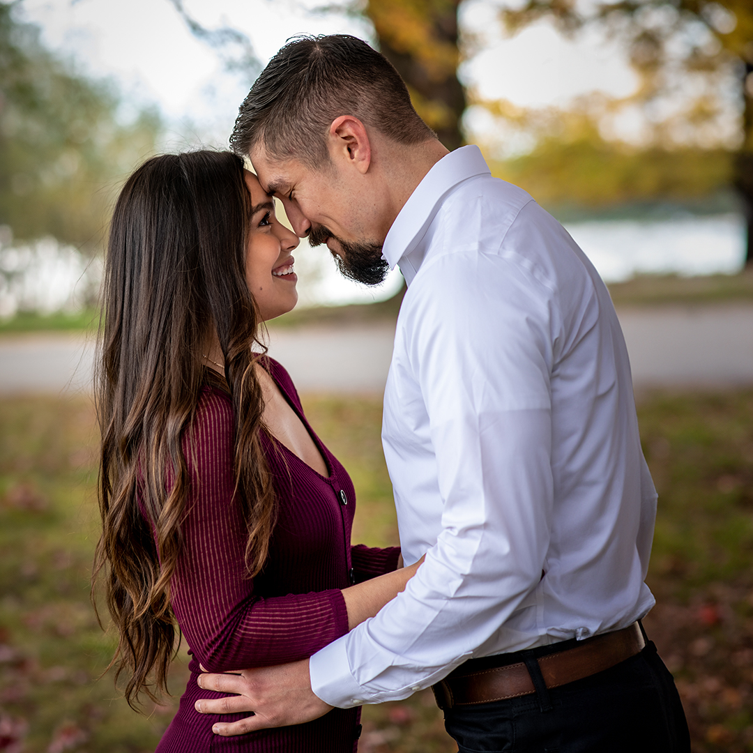 Man and his fiancé stand facing each other with foreheads touching. 