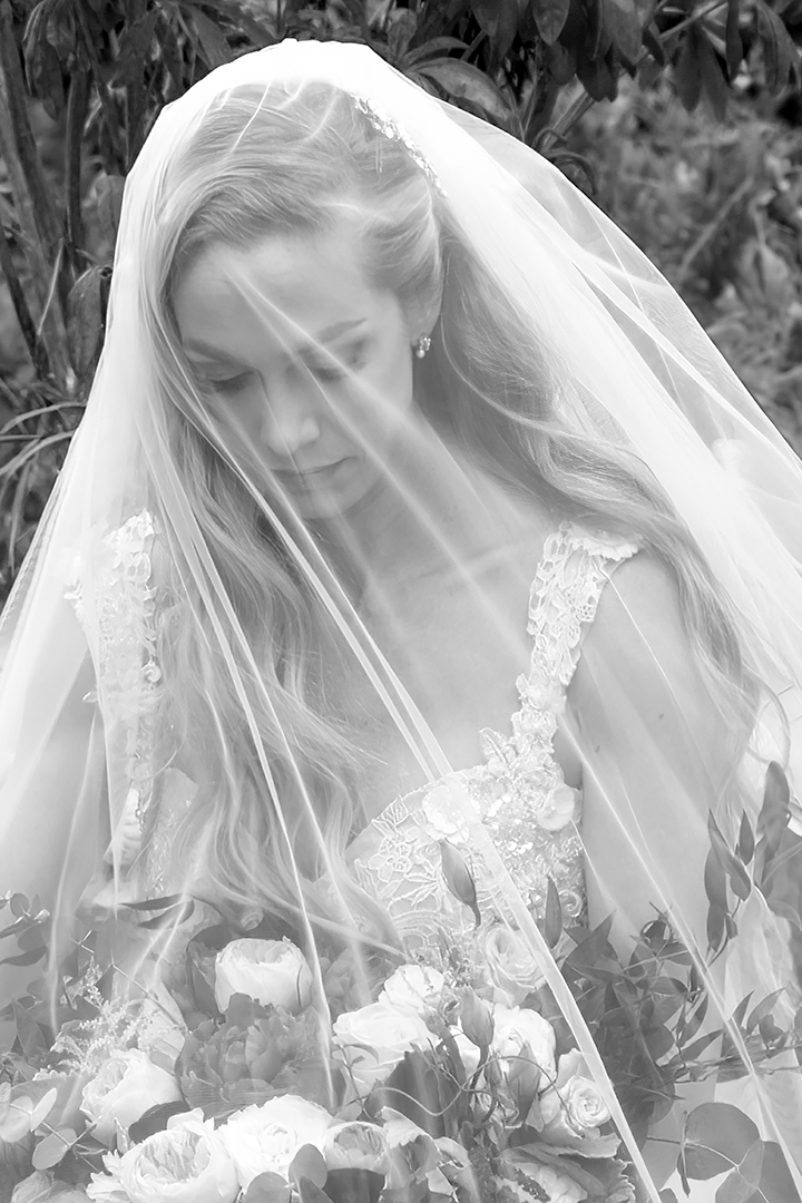 A PNW bride is under a cathedral length veil looking down. The photo is in black and white. The bride's handmade floral bridal gown is white. 