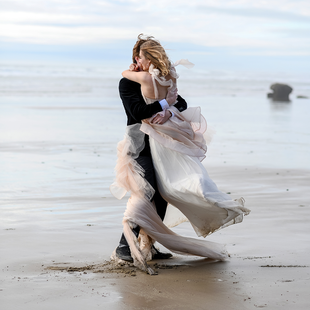 Couple celebrates their wedding Olympic Peninsula. The wind blows through their hair and wraps the bride's dress around the rooms legs as he sings her around. 