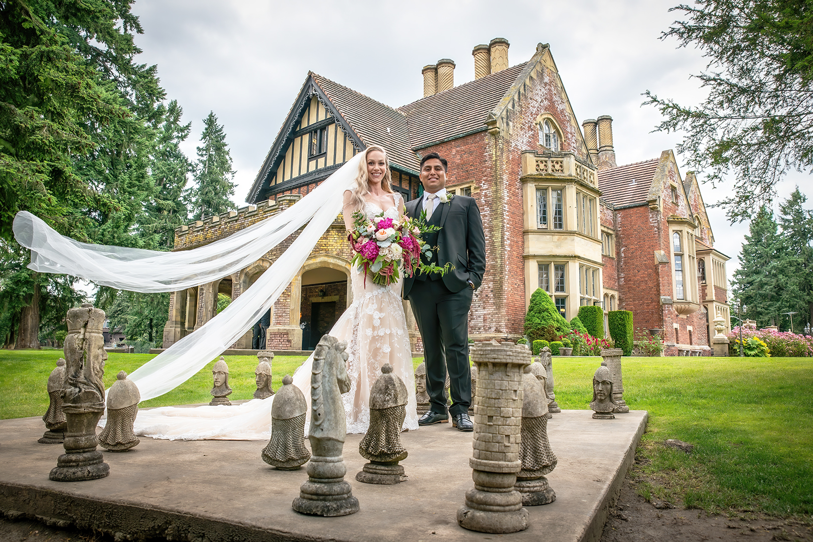 Bride and groom standing on a life-size chess board. Bride is holding a cascading bouquet while the breeze caught her cathedral length veil near Portland. 