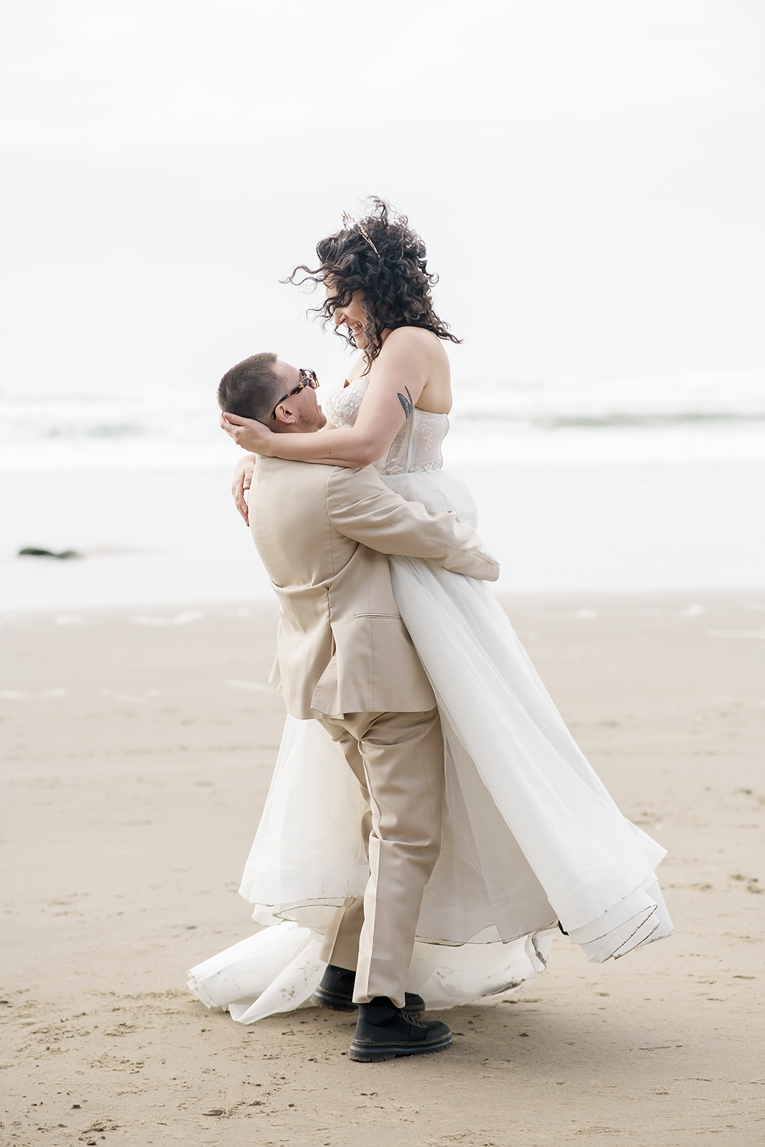 Groom lifts the bride on the beach. The wind caught her hair. He's spinning her around. 