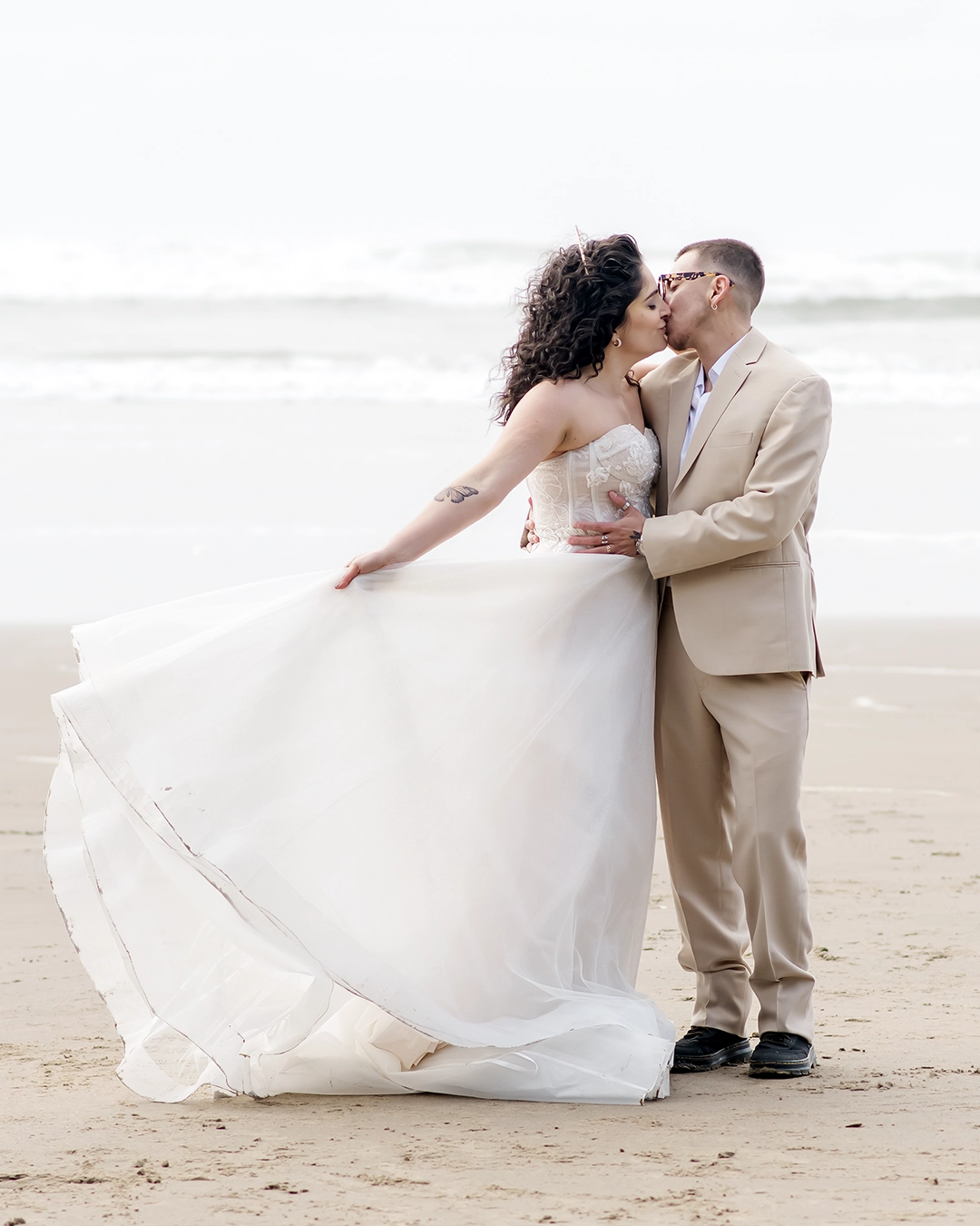 Bride swings her dress while kissing her groom on the sandy beach in Oregon. 