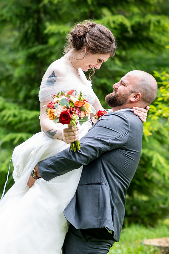 Couple embraces as a groom lifts his bride up on their wedding day. Both smile at each other as he spins her around.