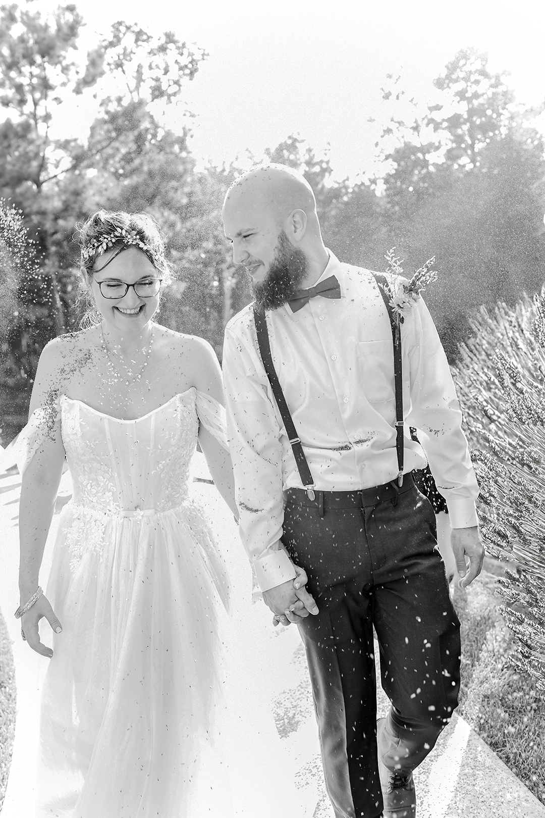 Bride and groom smile while walking hand n hand as guests toss lavender at them on their grand exit. 