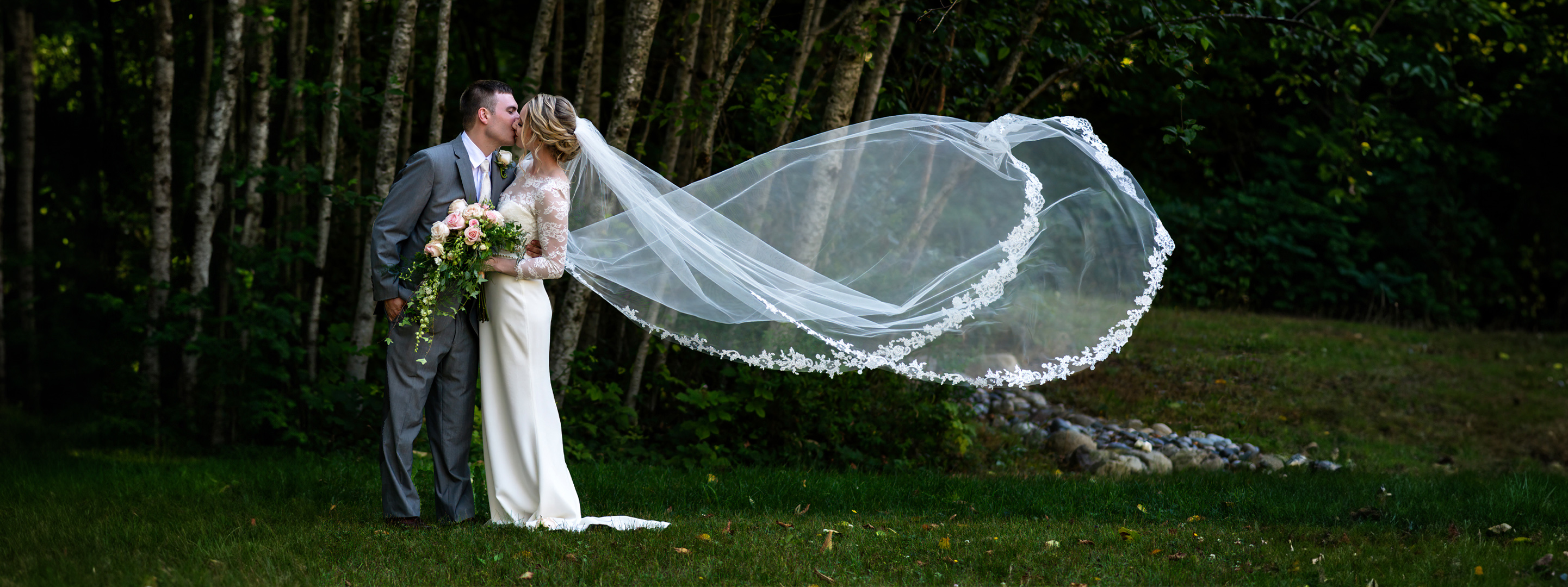 couple portraits with the backdrop of a row of trees while the veil falls in the wind.