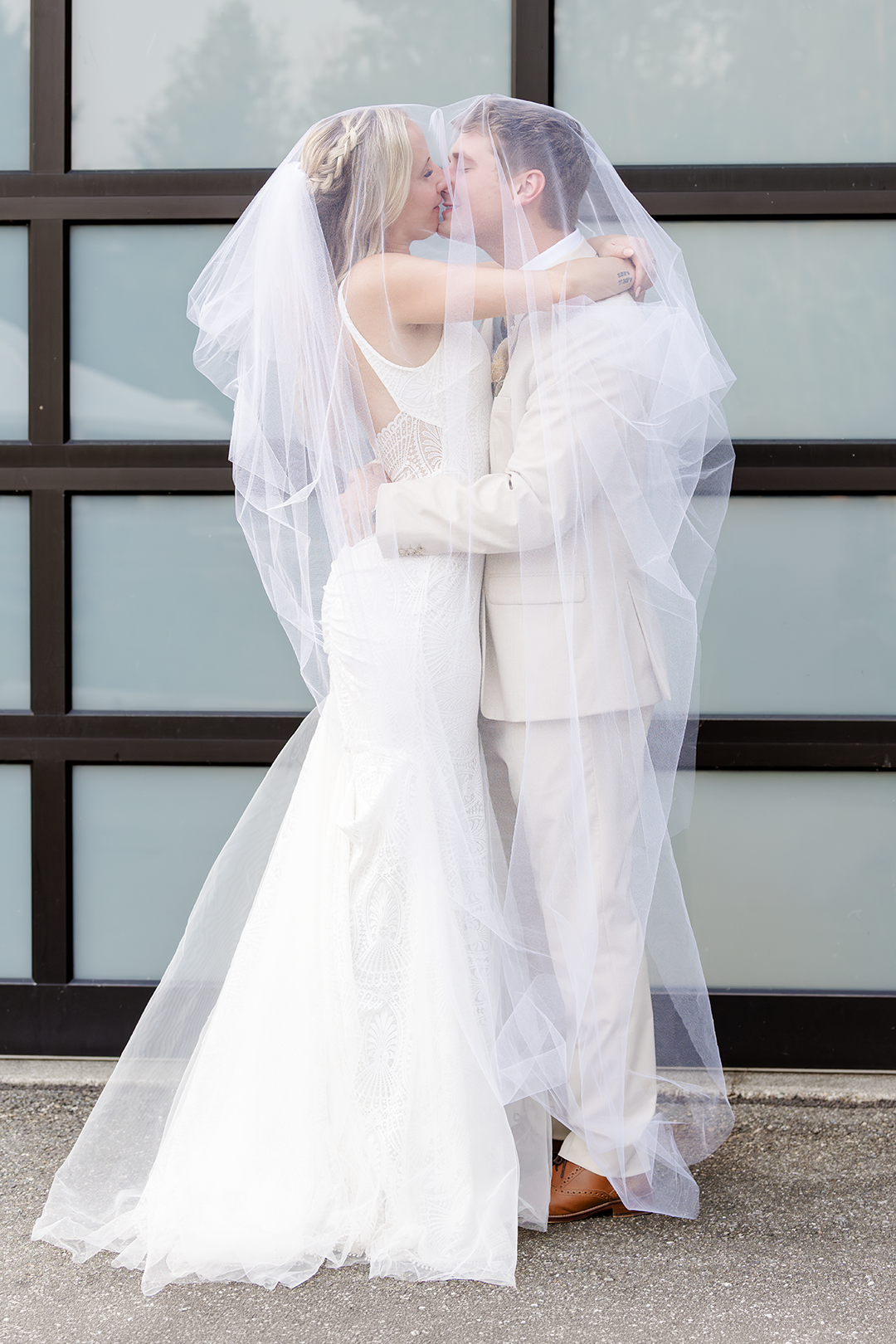 Couple starts to laugh and kiss under the veil during couple portraits on their wedding day.