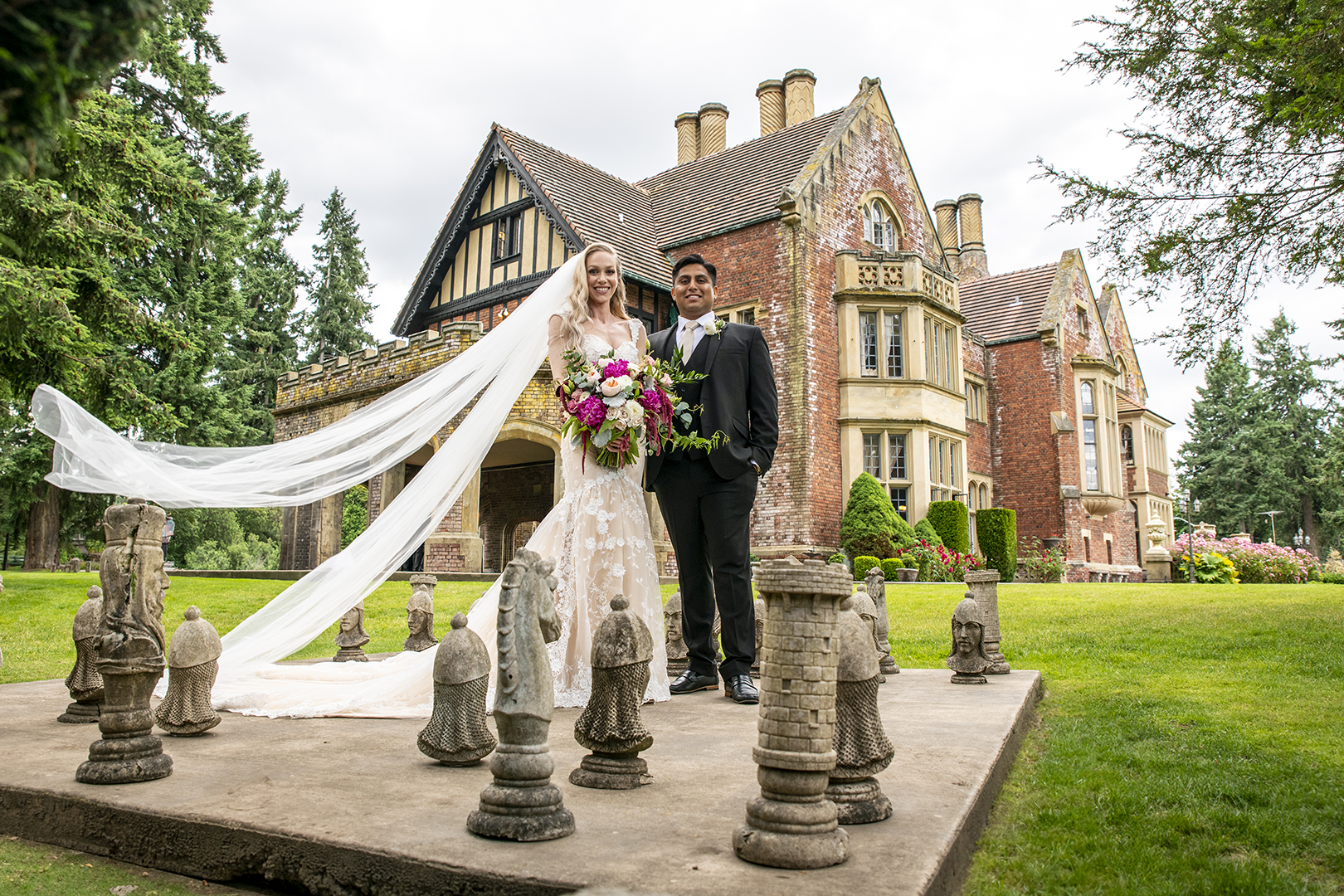 Couple stands on the life-sized chess board with Thornewood Castle in the background on their wedding day. 