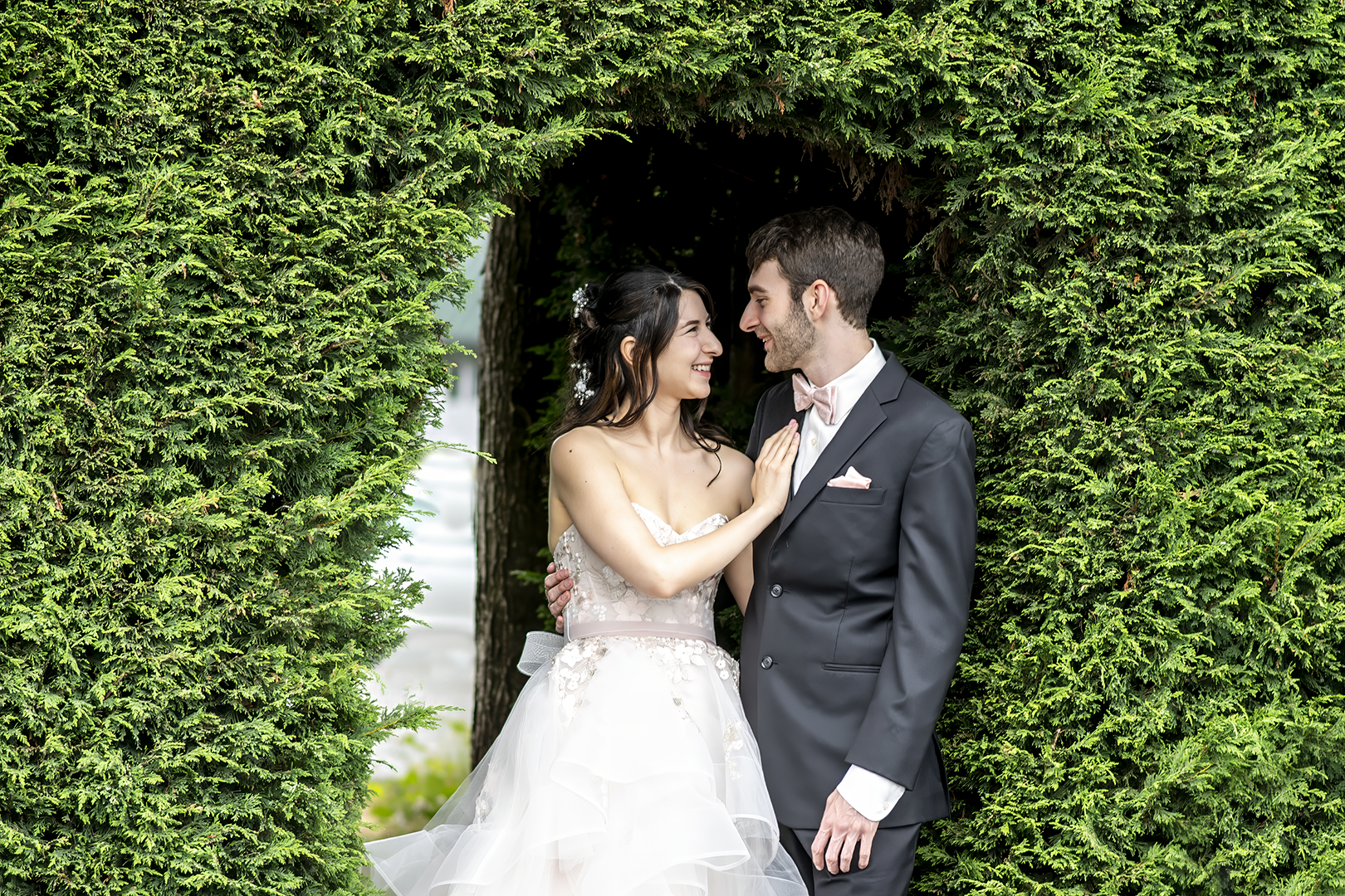 Couple stands in an opening in a evergreen hedge at the Willows Lodge.