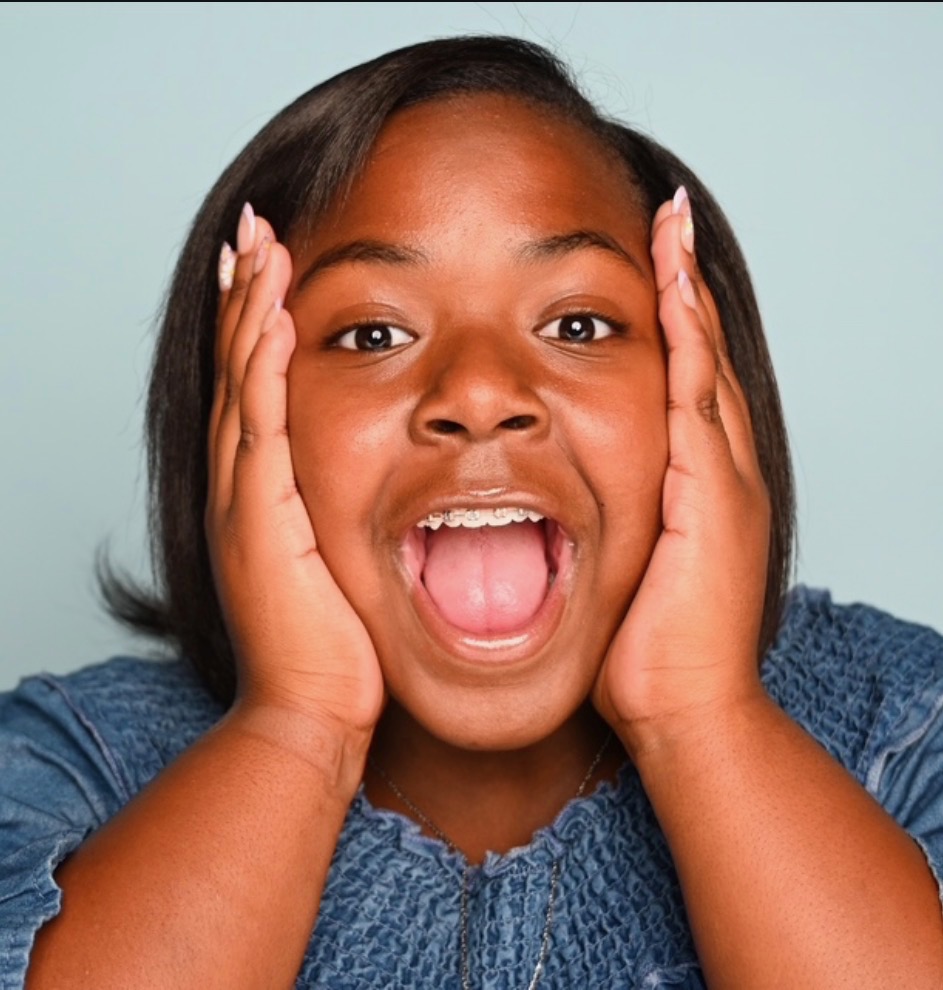 Tyli Joy Gilmore, hands on cheeks, mid-gasp in a denim top