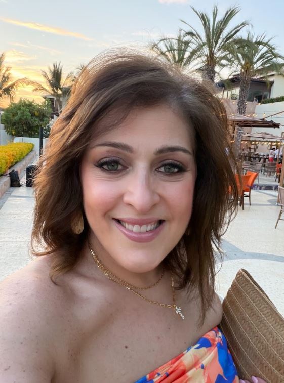 Anna Gibbs smiling, with palm trees and the resort behind her in Aruba