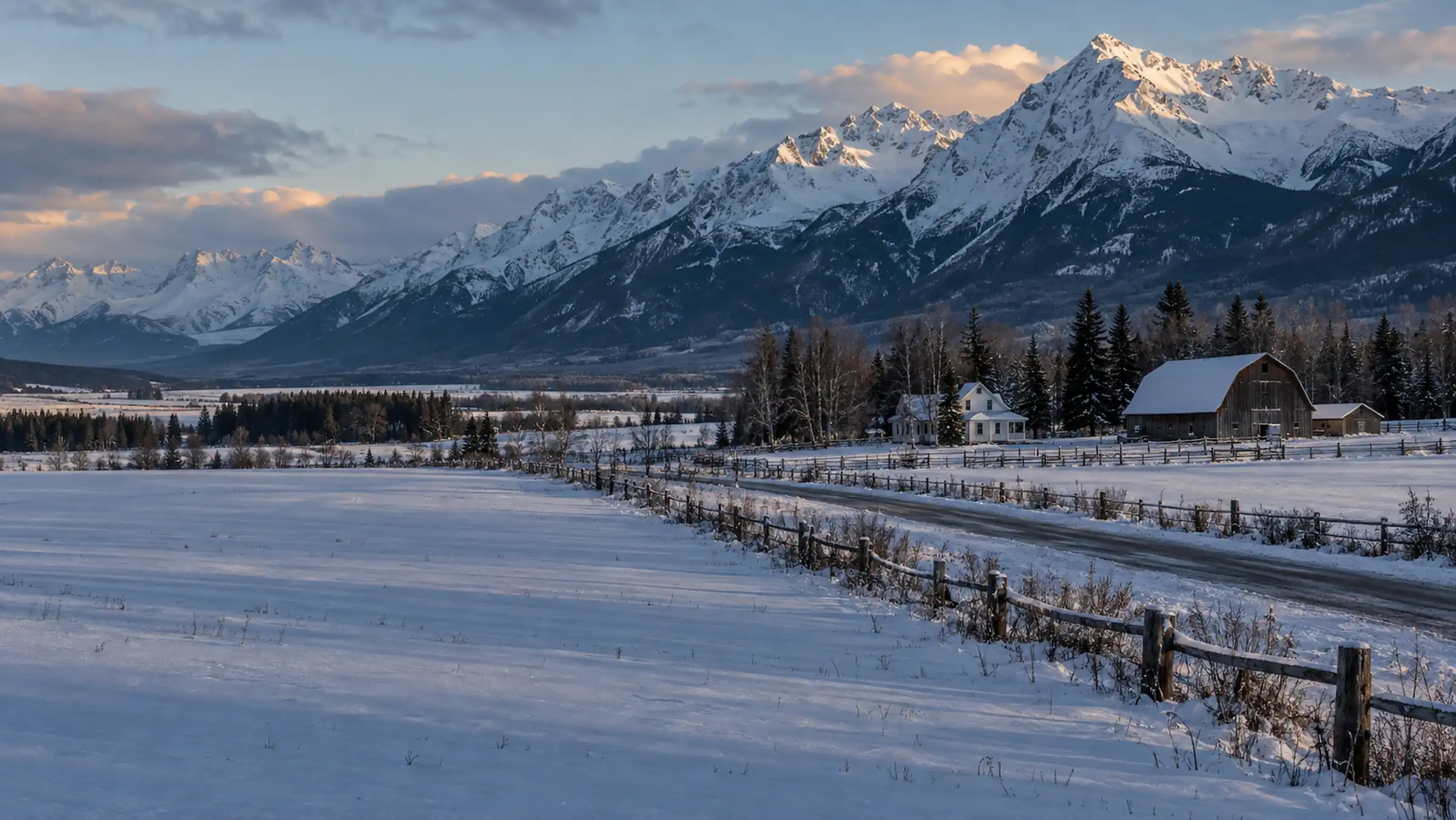A white farmhouse and weathered gambrel barn beside snow-covered fields and fence lines below the Chugach Mountains in the Matanuska Valley, Alaska