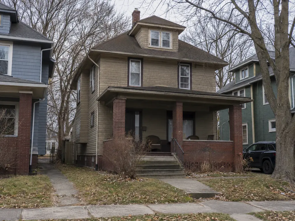 Pre-1940 American foursquare house with a full-width brick porch on a Cleveland street, the kind of older home we buy as-is