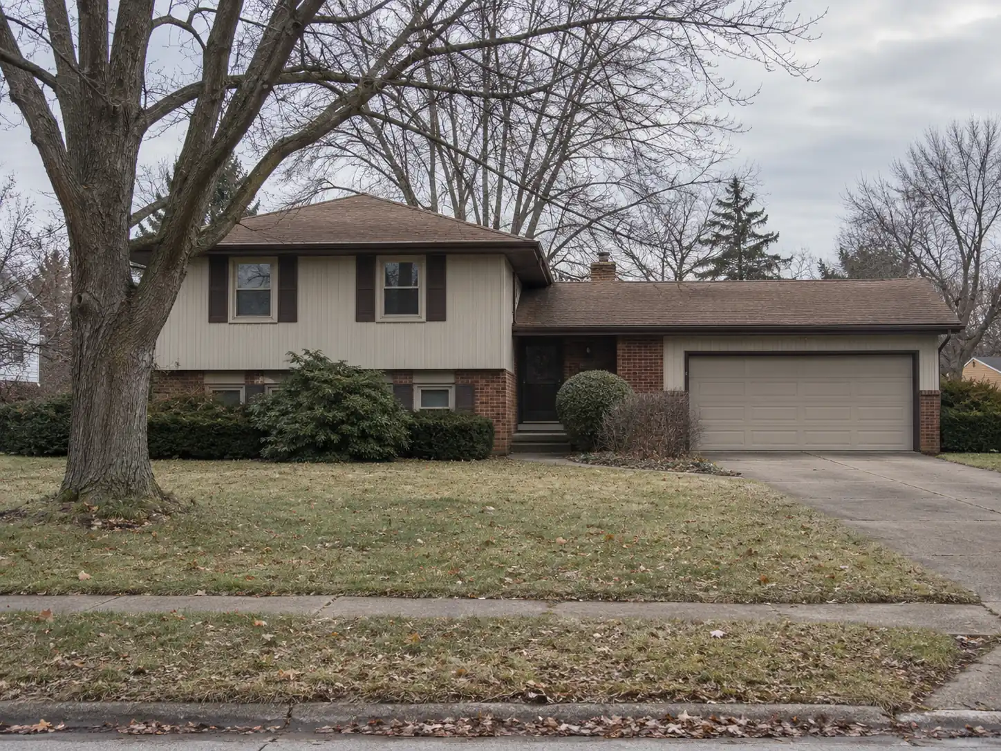 1970s split-level suburban house with an attached two-car garage and mature maple in a Cleveland suburb