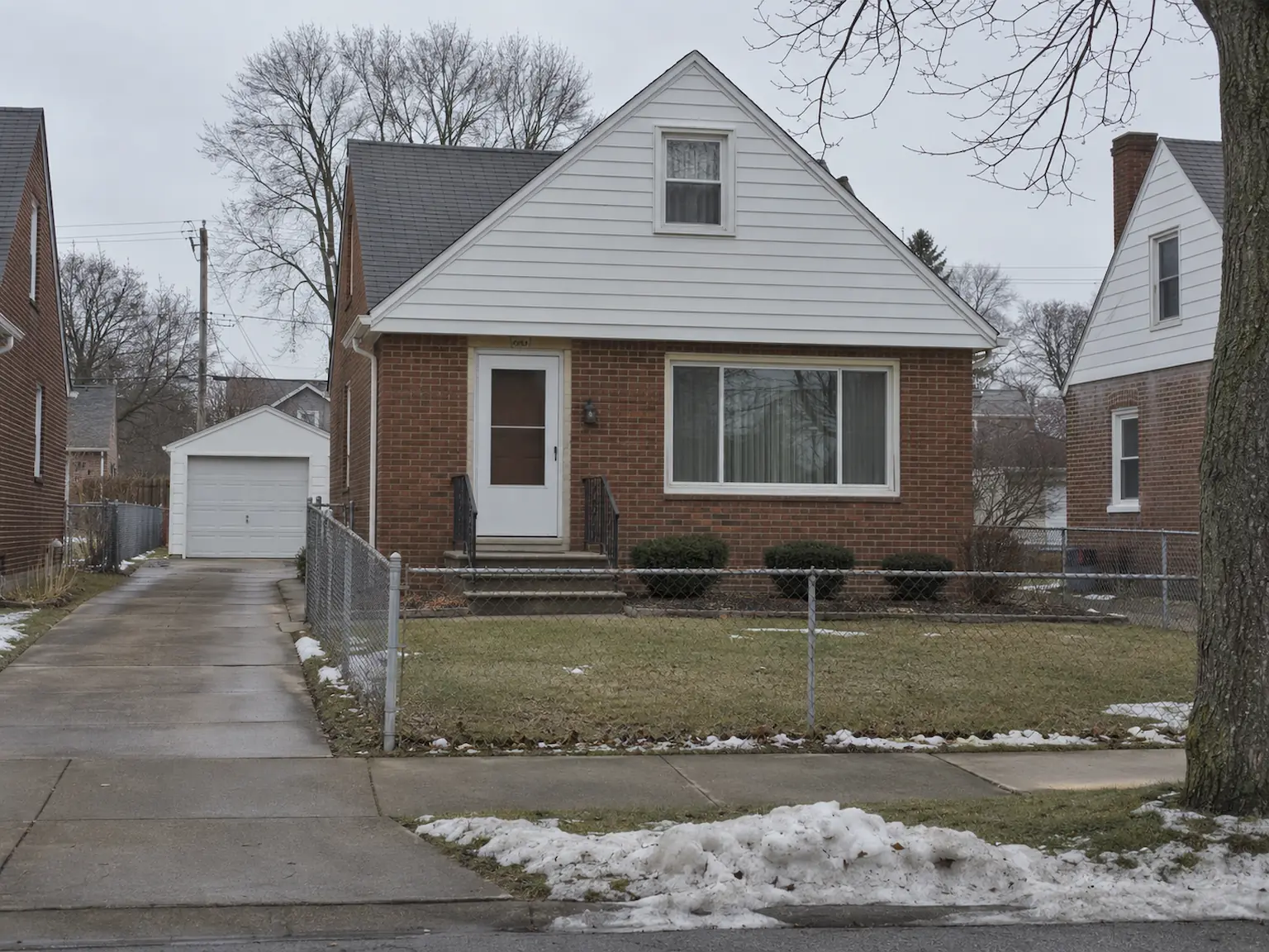 Brick Cape Cod house in Parma, Ohio with a front dormer, picture window and detached garage down a narrow side driveway