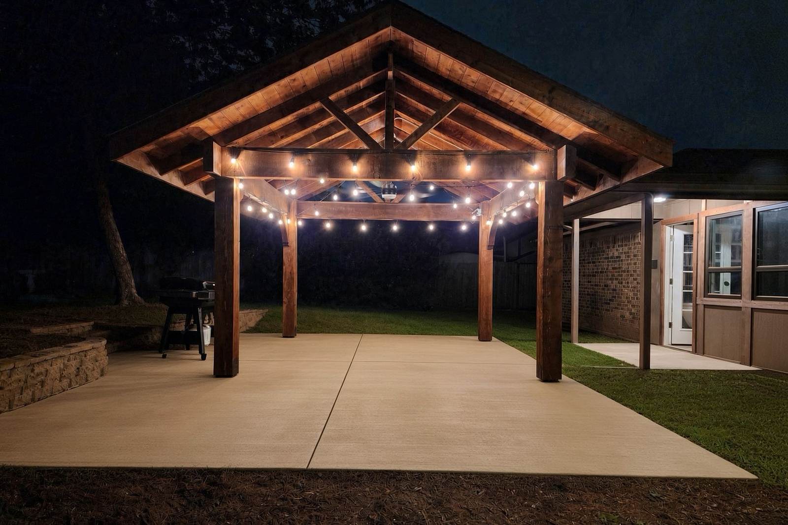 Cedar pavilion with string lights over a new concrete patio at night