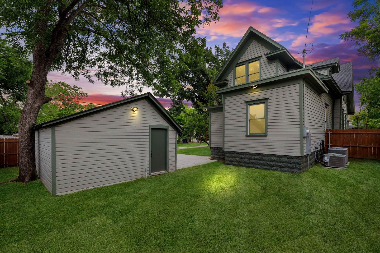 Rebuilt historic Fort Worth home at dusk with new windows lit and a rebuilt garage