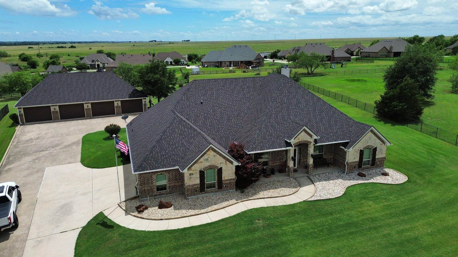 Aerial view of a large brick home with a new dark architectural shingle roof and three-car garage, replaced by Zeus Exteriors
