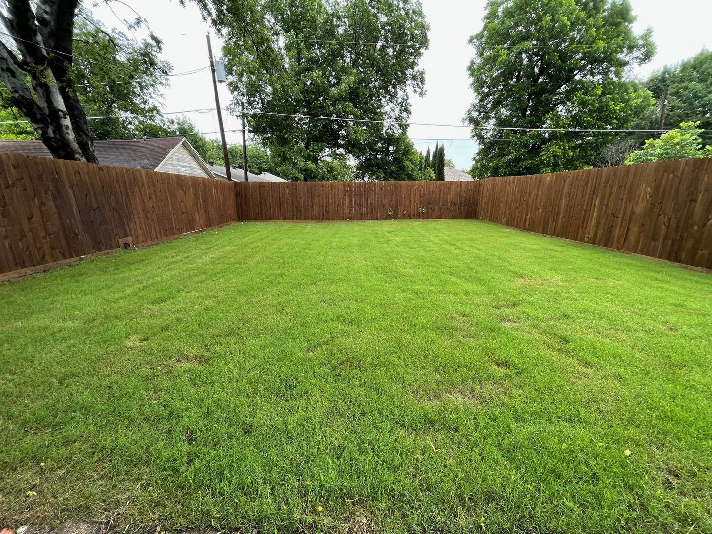 New stained board-on-board wood privacy fence around a green backyard in North Texas