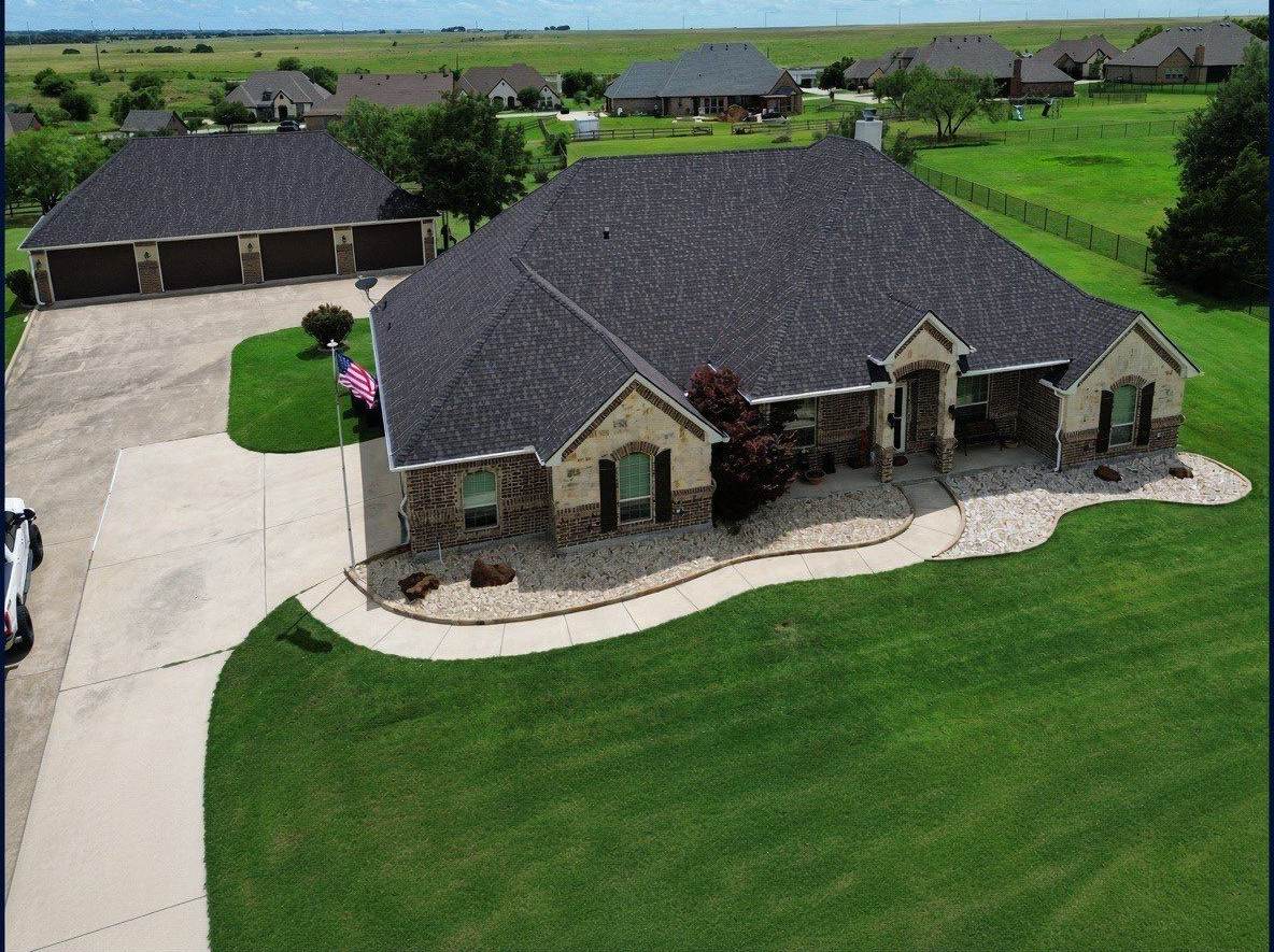 Front aerial view of a brick home with a newly replaced dark shingle roof