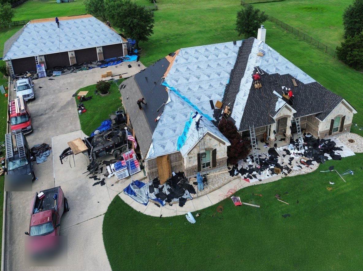 Roofing crew tearing off old shingles and laying new underlayment on a large home