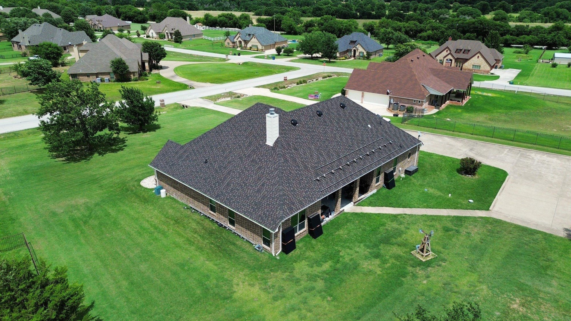 Rear drone view of a finished dark shingle roof on a brick home with a chimney in Farmers Branch, TX