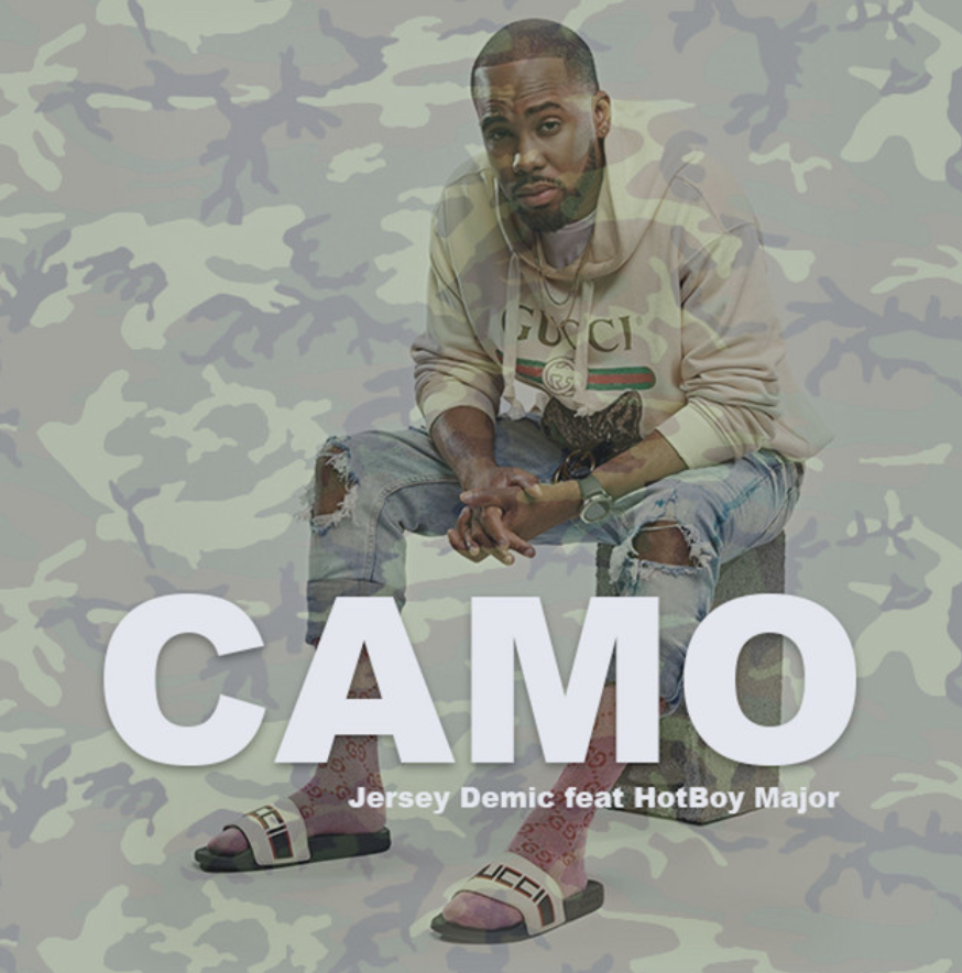 Man in designer clothing seated against a camouflage background, promoting the song "Camo" by Jersey Demic featuring HotBoy Major.