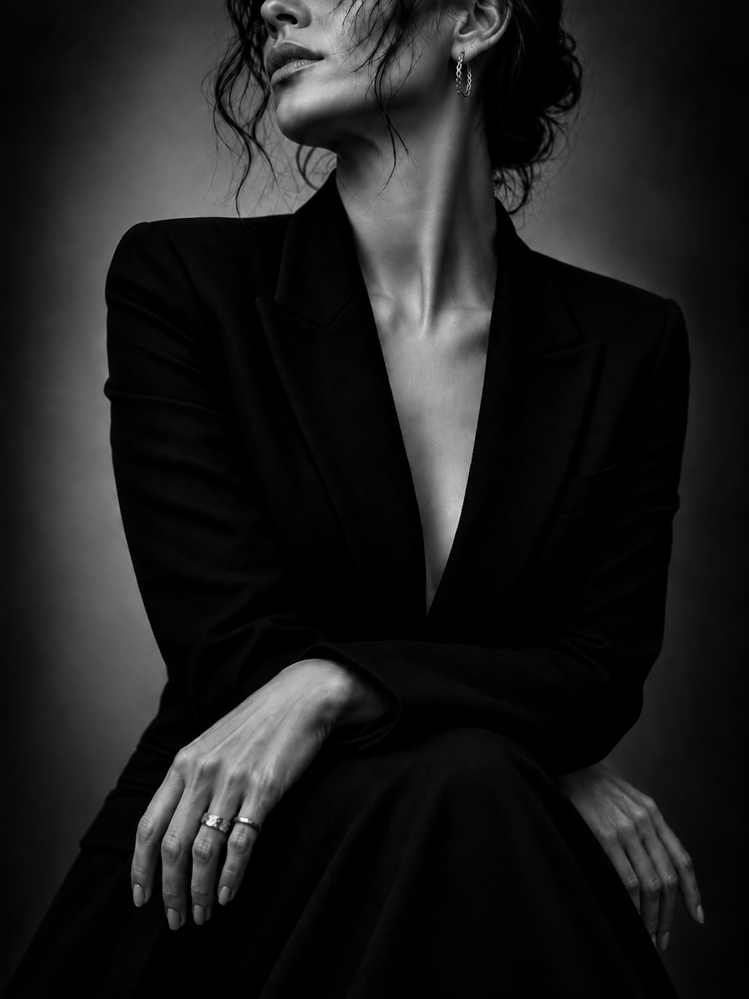 Black and white portrait of a woman in a tailored blazer, seated with her hands clasped, gold jewellery visible