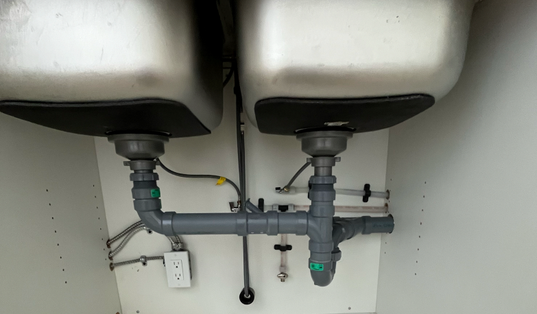 Under-sink plumbing with PEX supply lines clipped to the cabinet back and push-fit waste pipework
