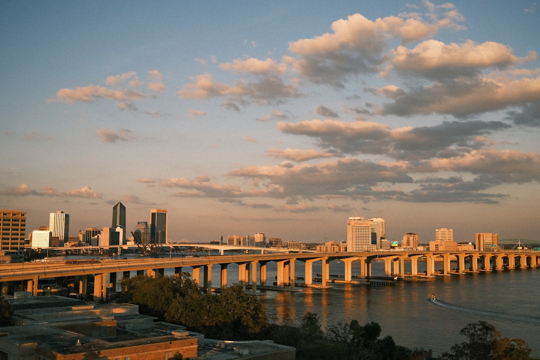 Jacksonville, Florida downtown skyline at sunset across the St. Johns River with a long highway bridge in the foreground.