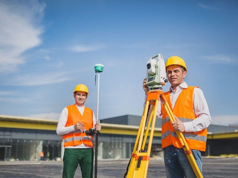Land surveyors using a GNSS rover and total station to collect ground control measurements at a construction site Land surveyors using a GNSS rover and total station to collect ground control measurements at a construction site