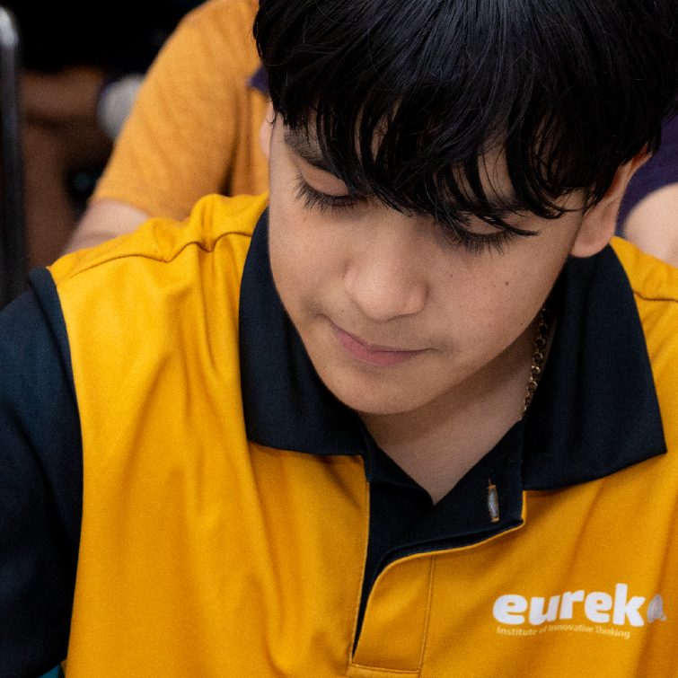 Alumno de Eureka con playera amarilla del instituto concentrado escribiendo en clase
