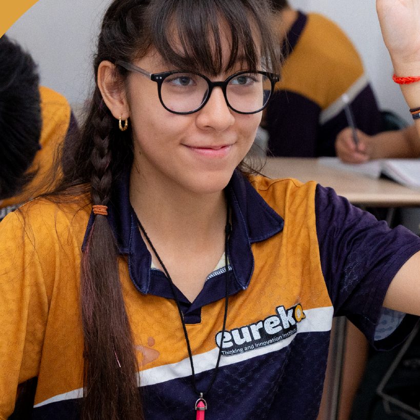 Alumna de Eureka con lentes levantando la mano en clase
