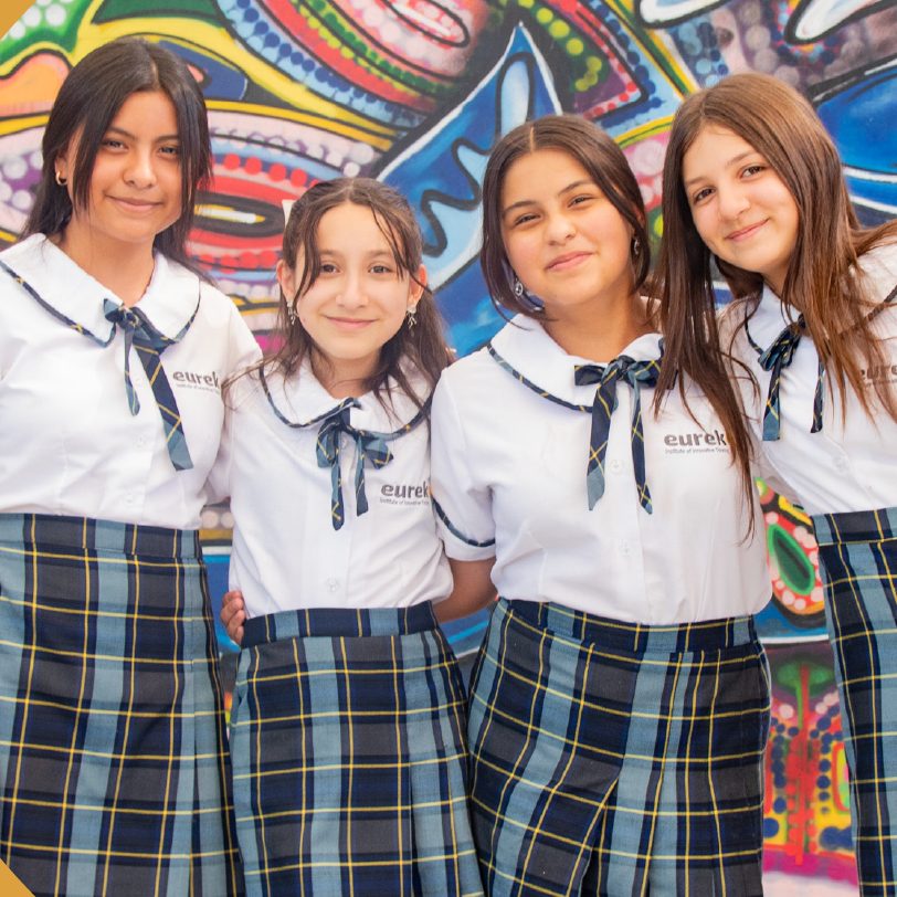 Cuatro alumnas de Eureka con uniforme de falda escocesa, sonriendo frente a un mural
