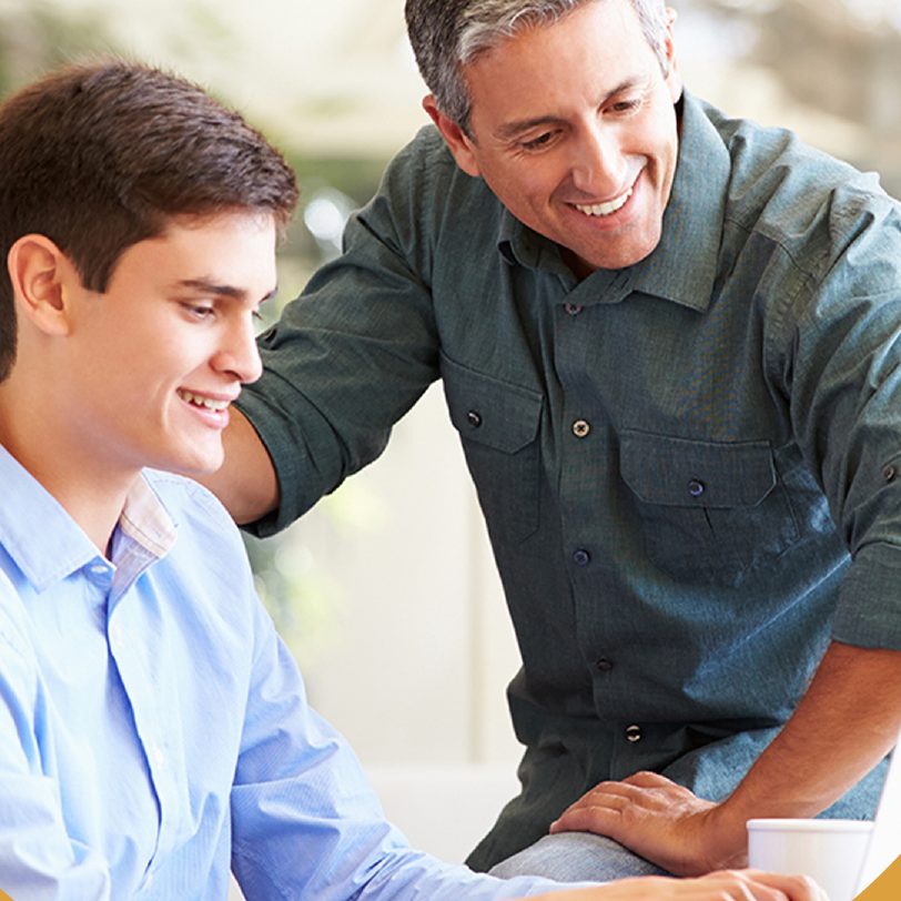 Padre e hijo sonriendo mientras revisan un trabajo en la computadora