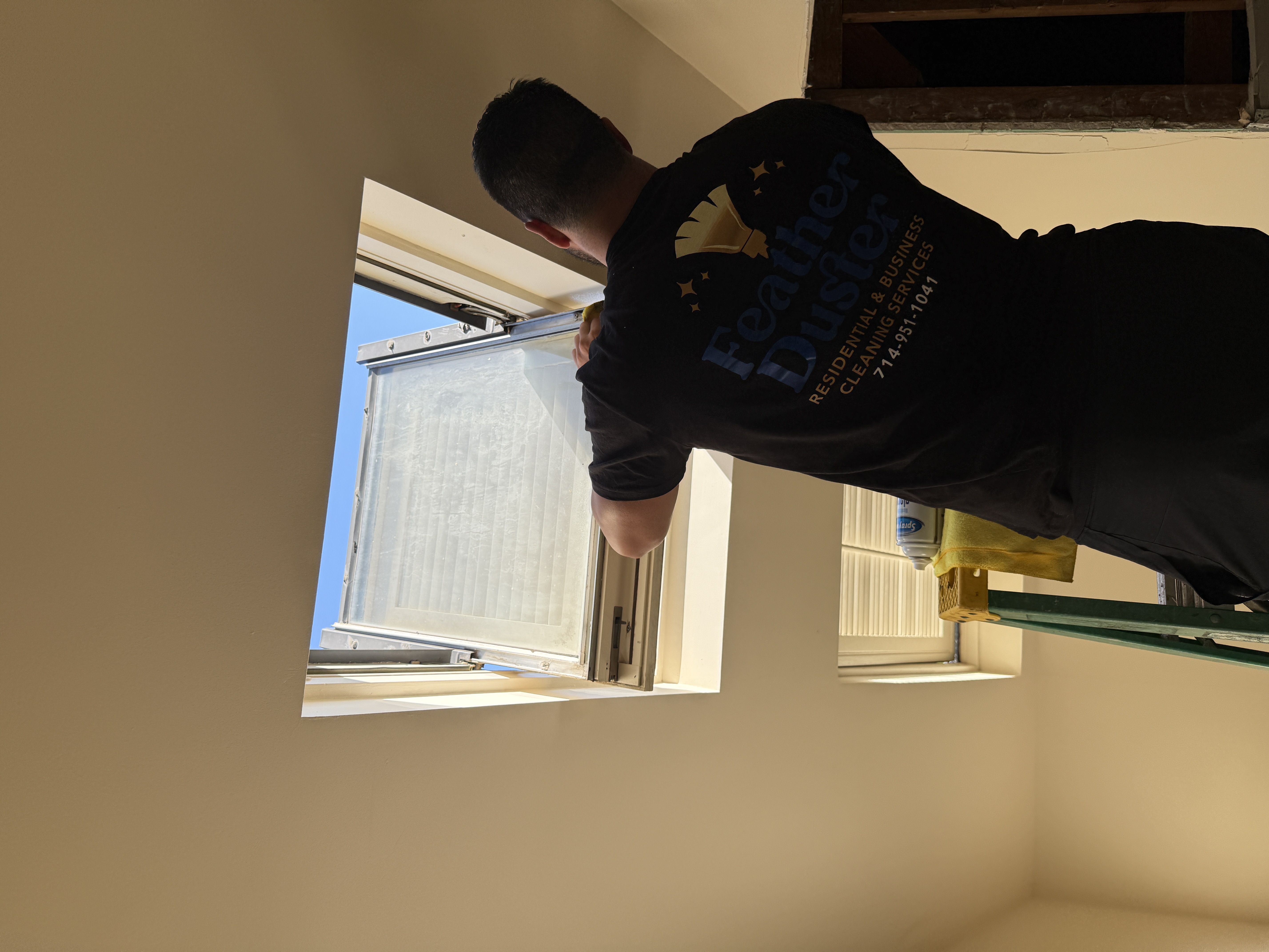 Feather Duster team member cleaning a residential skylight from a step ladder