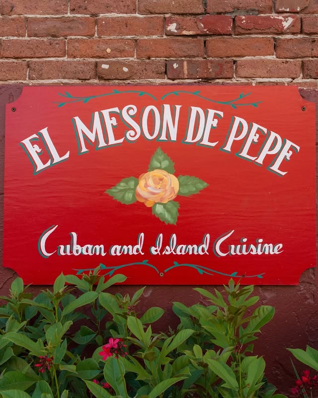 El Mesón de Pepe sign highlighting Cuban and island cuisine, adorned with a rose and surrounded by vibrant foliage.
