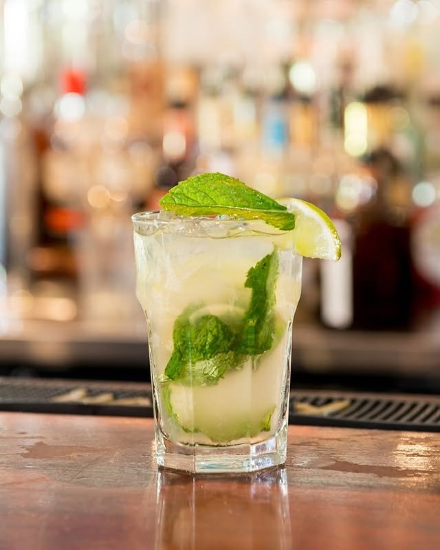 Refreshing mojito garnished with mint and lime, showcasing El Mesón de Pepe's signature cocktail in a vibrant bar setting.