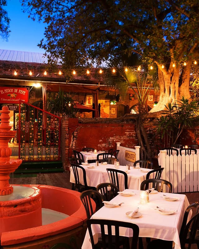 Charming outdoor dining area at El Mesón de Pepe, featuring tables, a pink fountain, and tropical ambiance in Key West.