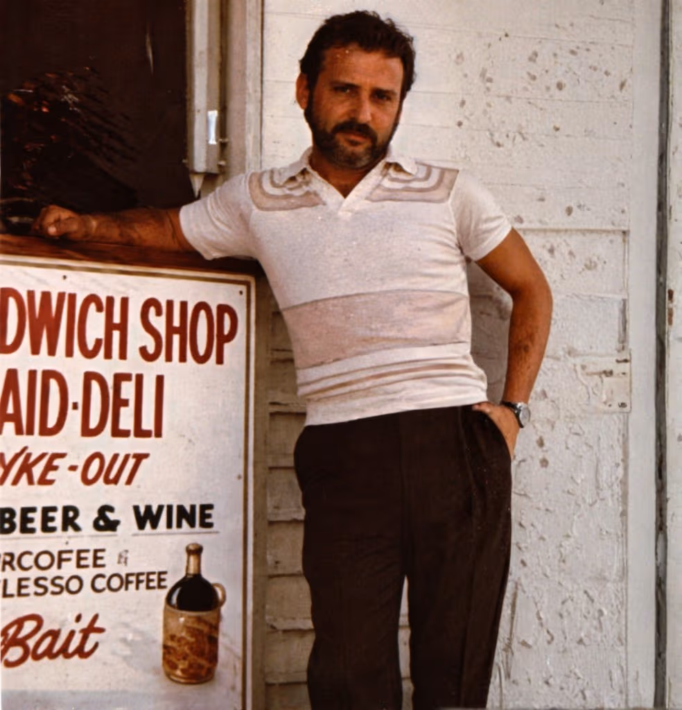 José "Pepe" Diaz, Key West founder, stands near a historic sandwich shop sign.
