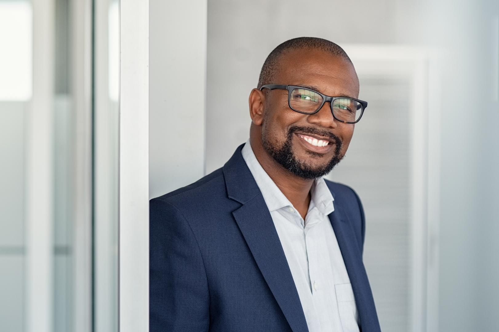 Smiling professional man in a suit holding eyeglasses in a bright office hallway