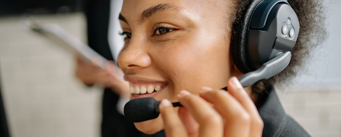 Smiling customer support professional wearing a headset and assisting a caller at a desk