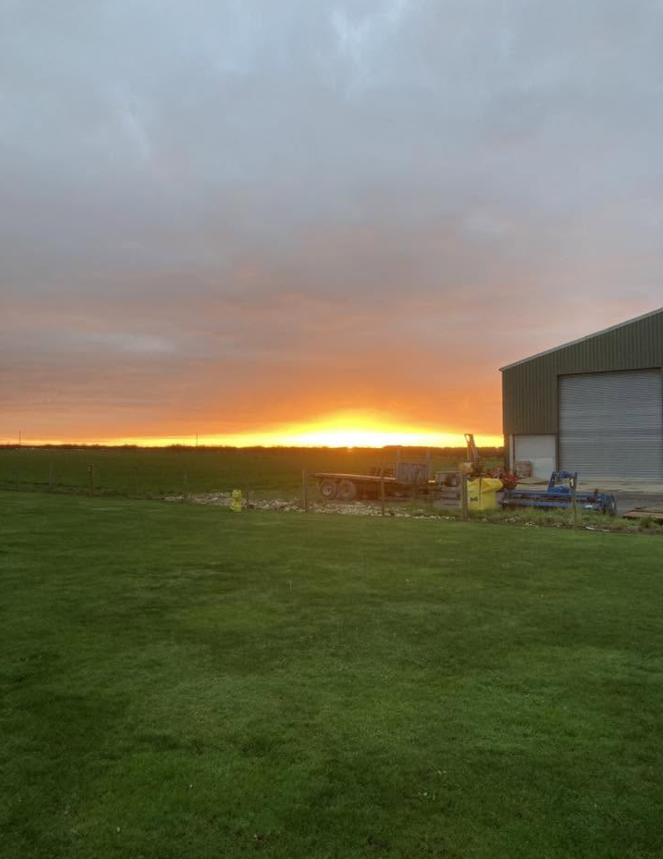 Sunset over the fields beside a farm barn and machinery