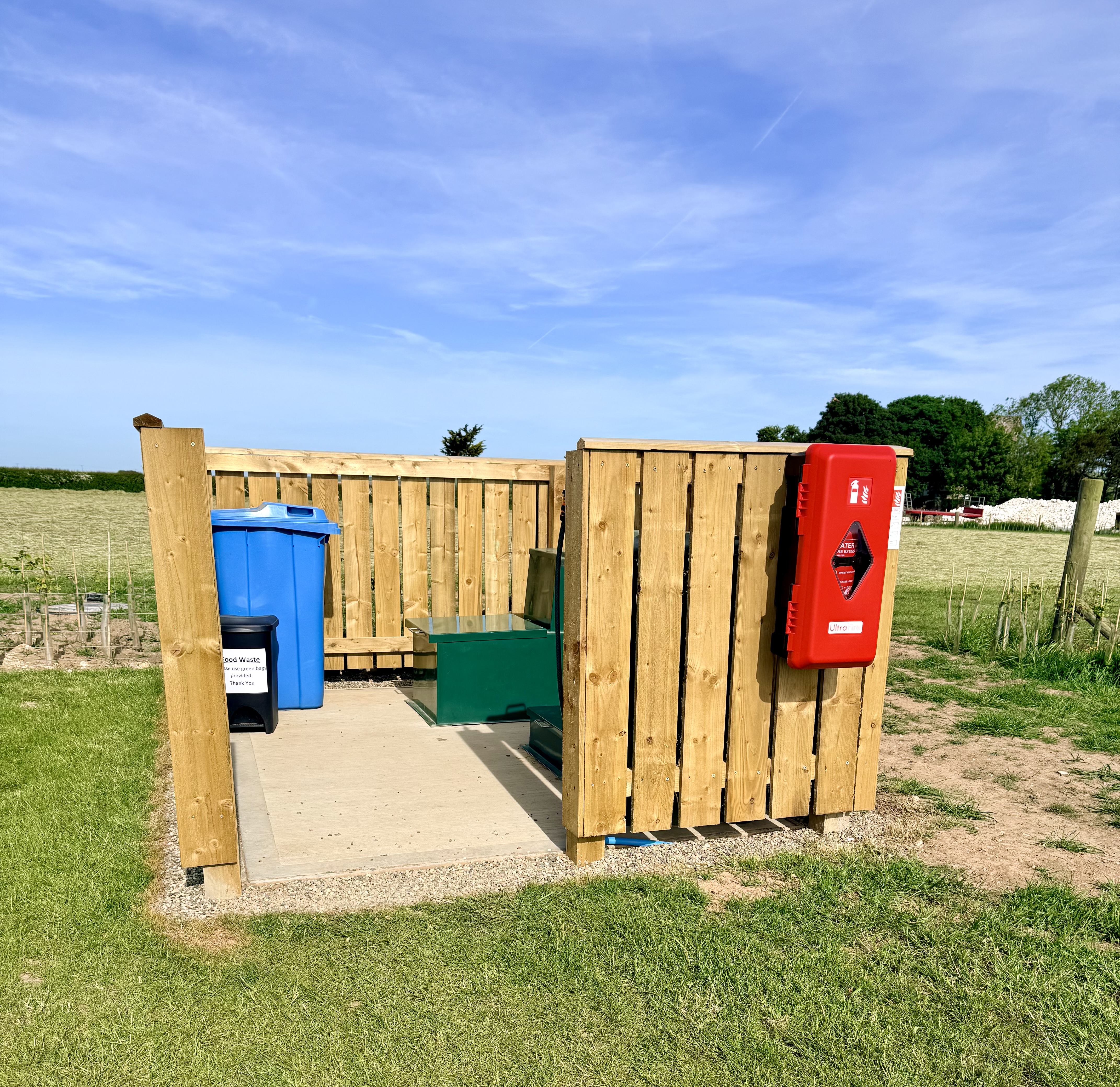 Wooden-fenced facilities area with recycling bins and a fire point