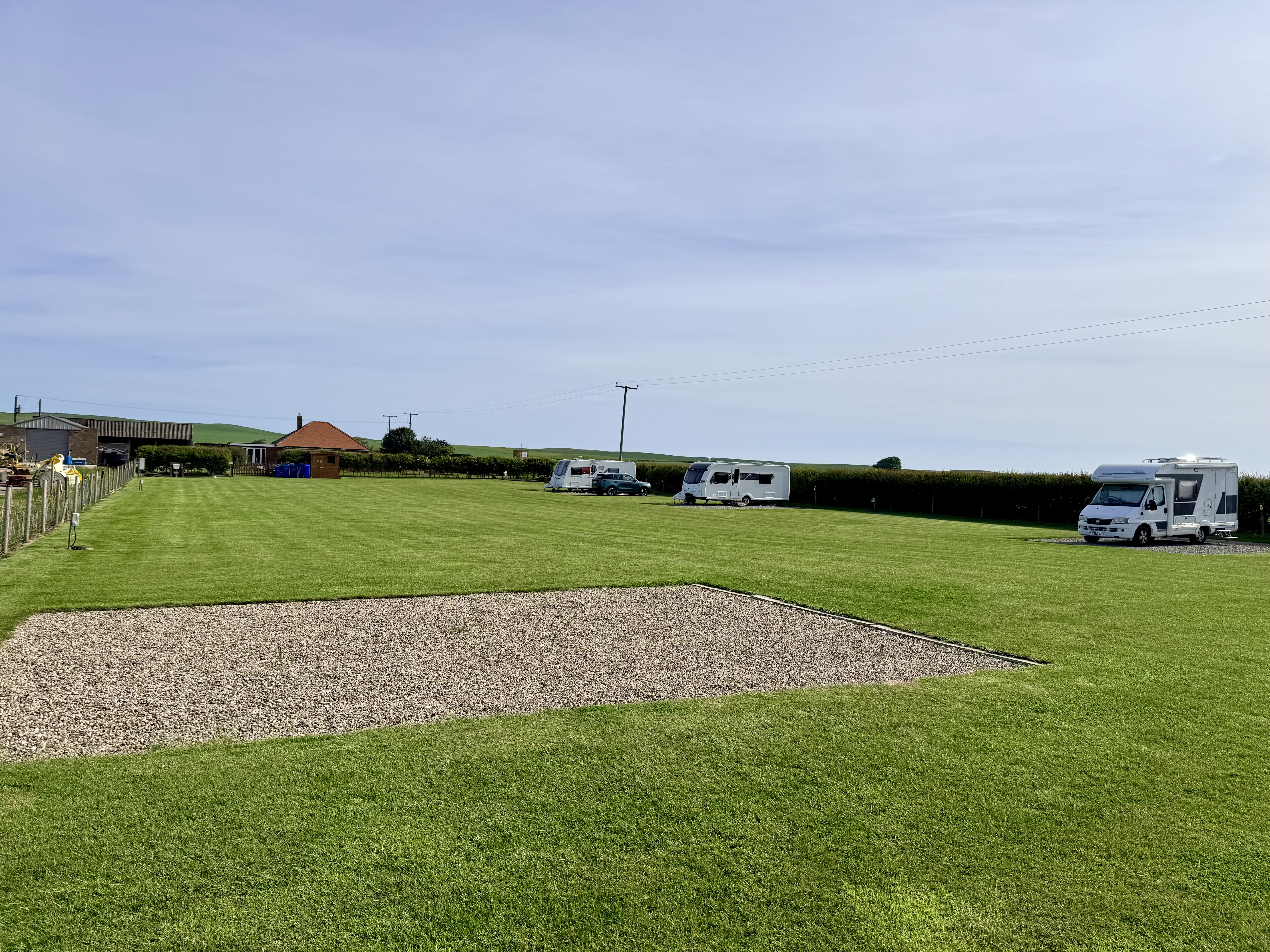 Gravel hard standing pitch on a level, mown grass field with caravans beyond
