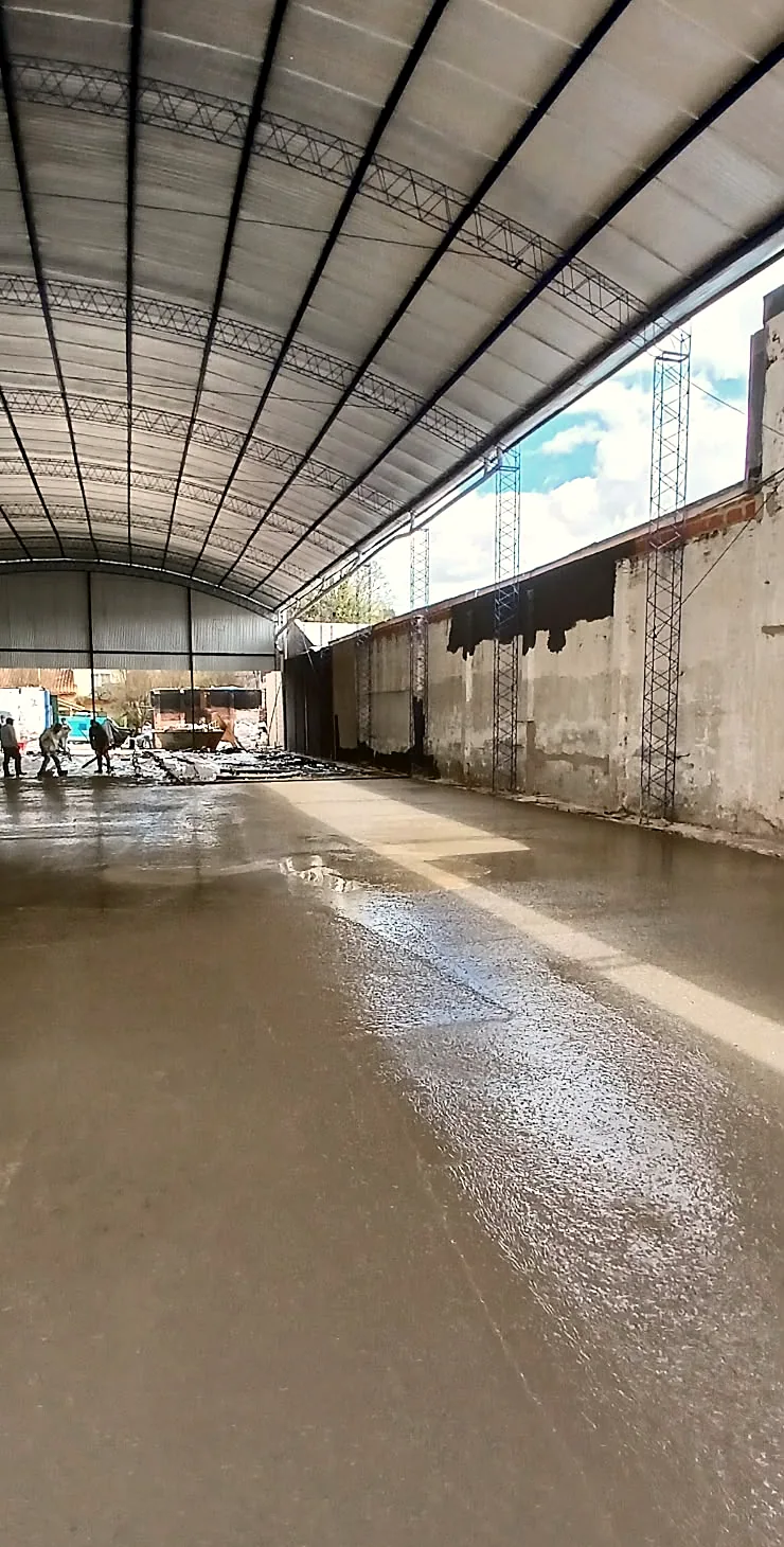 Vista a lo largo de un galpón con cubierta curva y el piso de hormigón recién colocado.