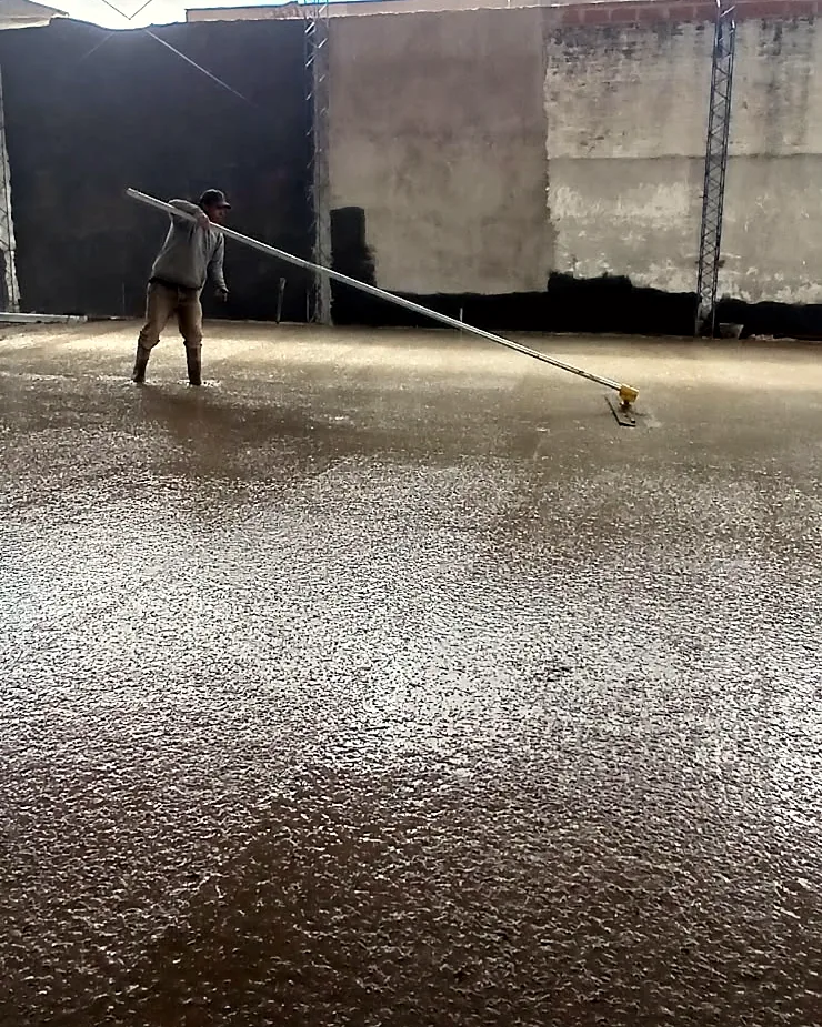 Operario alisando el hormigón con una herramienta de mango largo frente al muro del fondo.