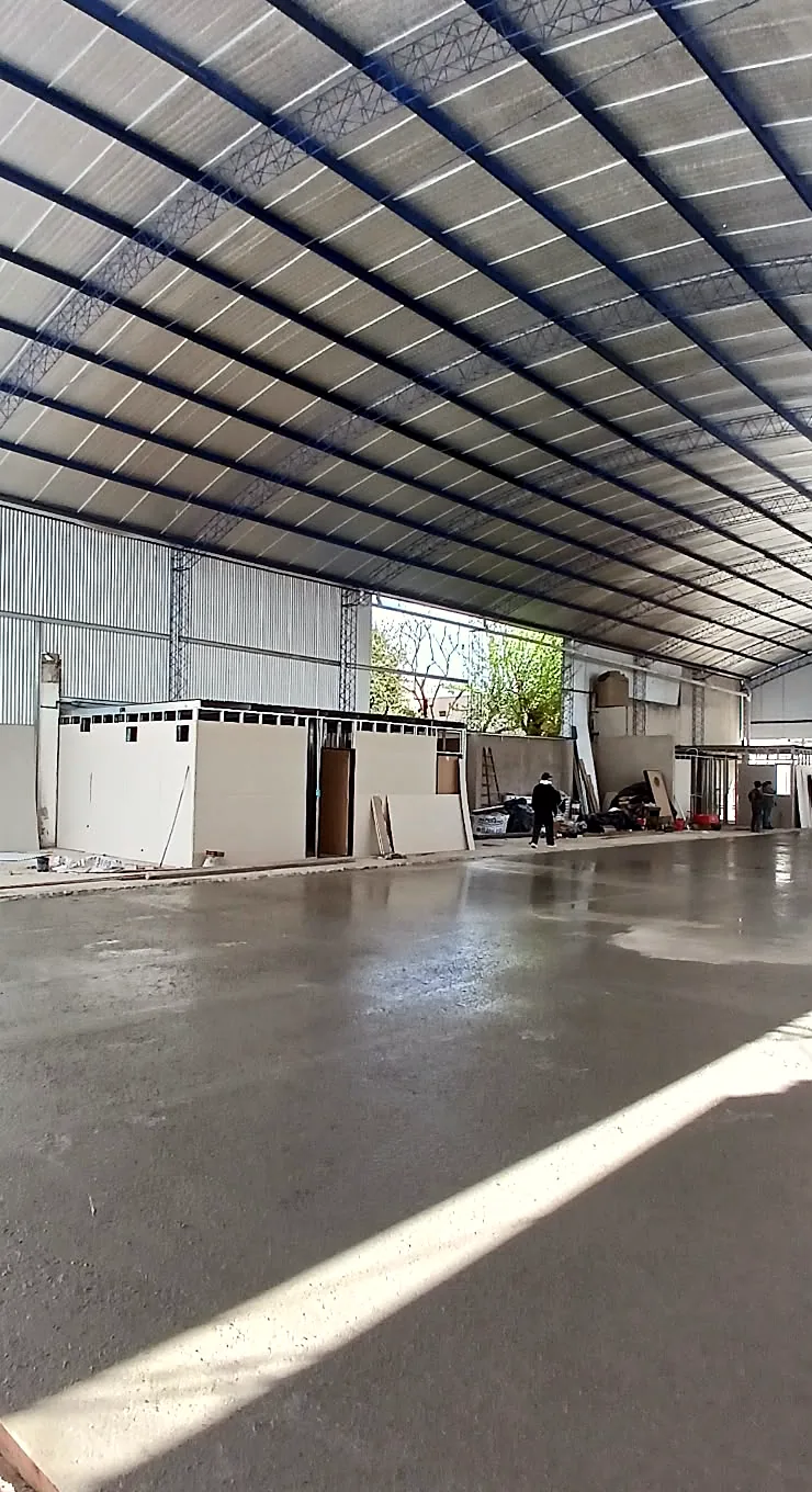 Interior de un galpón con cubierta curva: el piso de hormigón recién hormigonado y un haz de luz natural que cruza la superficie.