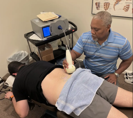 Dr. Gerdine applying a shockwave handpiece to a patient's lower back
